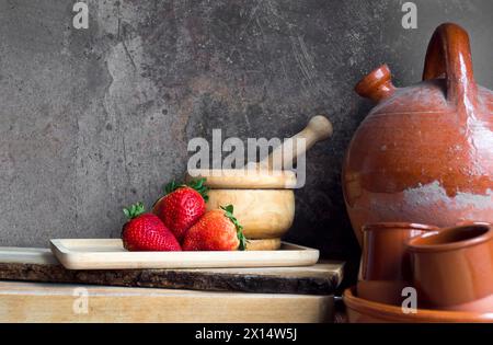 Erdbeeren auf einem Holztablett neben einem alten Botijo und anderen Keramik- und Holzutensilien Stockfoto