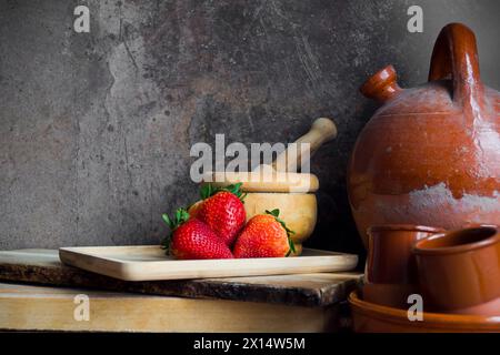 Erdbeeren auf einem Holztablett neben einem alten Botijo und anderen Keramik- und Holzutensilien Stockfoto