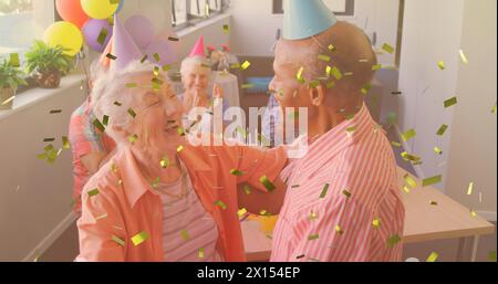Goldenes Konfetti, das gegen das kaukasische Seniorenpaar fällt, das während der Geburtstagsfeier zusammen tanzt Stockfoto