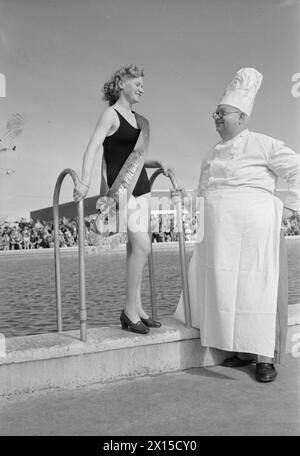 DAS FERIENLAGER GEHT WIEDER LOS: DER ALLTAG IN EINEM BUTLIN'S FERIENLAGER, FILEY, YORKSHIRE, ENGLAND, GROSSBRITANNIEN, 1945: Miss Joan Shepherd aus Whitstable in Kent steht neben dem Pool in der Sonne im Butlin's Holiday Camp, Filey, und spricht mit einem der Campingköche. Miss Shepherd trägt einen Gürtel über ihrem Badekostüm, der sie als Siegerin beim „Holiday Lovelies“-Wettbewerb ausweist Stockfoto