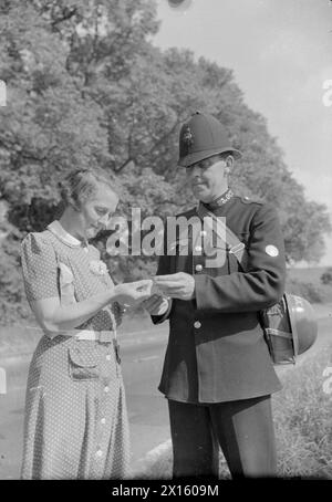 IN LEWKNOR, OXFORDSHIRE, ENGLAND, 1941 - Mrs Scott, die Dorfschulmeisterin, verkauft Sparmarken an den örtlichen Polizisten PC Hufton auf einer sonnigen Landstraße. PC Hufton ist ein ehemaliger Wachmann Stockfoto