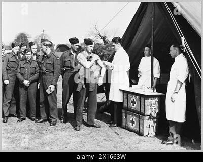 AUF Einer T.A.F.-STATION IN GROSSBRITANNIEN - Bild von einer Tactical Air Force Station in Großbritannien (ausgestellt 1944) zeigt - nur ein Teil unseres Dienstes. Flieger der 2. Taktischen Luftwaffe erhalten Impfungen in einem mobilen Krankenquartier, damit sie, wenn sie die „andere Seite“ erreichen, Keimen und Deutschen widerstehen können. Die Hypodermie ist Flight Lieutenant V.C.Walker, ein australischer Mediziner, der von dem führenden Luftfrachtmann J. Iredale aus Huddersfield und dem führenden Luftfrachtführer H. Wright aus der Southend-on-Sea Royal Air Force unterstützt wird Stockfoto