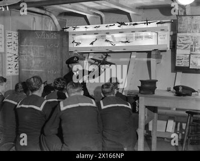 ENTWÄSSERUNG DES ROYAL NAVY-ZUGES AUF DEM MODERNEN SCHULSCHIFF. SEPTEMBER 1941 AN BORD DES ZERSTÖRER-DEPOT-SCHIFFES HMS TYNE. DIE DESTROYERMEN SIND AUSGEBILDET IN GESCHÜTZE, TORPEDOFEUER, U-BOOT-ABWEHR, SEEMANNSCHAFT UND SIGNALGEBUNG. ES WERDEN SCHIFFSMODELLE VERWENDET UND DIE BELEUCHTUNG IST SO ANGEORDNET, DASS SIE DIE EFFEKTE VON SCHEINWERFERN, STERNMUSCHELN UND GESCHÜTZBLITZEN ERZEUGT. - Der Instruktionsschützen, ein Durchsuchungsoffizier, nimmt eine Klasse von Zerstörern in Flugzeugnerkennung Stockfoto