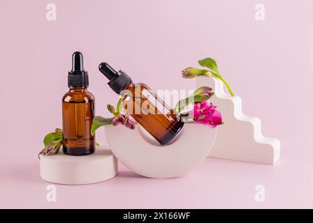 Zwei Tropfflaschen aus dunklem Glas mit einem Naturkosmetikum für Gesichts- und Körperpflege auf geometrischen Laufstegen mit Blütenknospen. Bio-Kosmetik Stockfoto