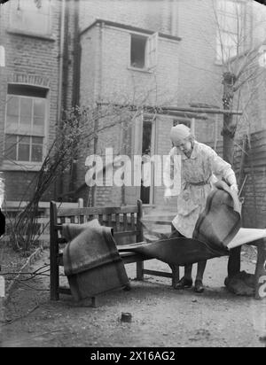 LONDON IM FRÜHJAHR 1941: ALLTAG IN LONDON, ENGLAND - diese Frau macht im Garten ihres Londoner Hauses eine Frühjahrsputzpause. Hier sehen wir, wie sie den Staub aus ihren Teppichen und Teppichen neben ihrer Gartenbank schlägt Stockfoto