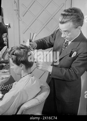 KRIEGSFRISEUR: DIE ARBEIT VON STEINER'S SALON, GROSVENOR STREET, LONDON, ENGLAND, GROSSBRITANNIEN, 1944 – im Steiner's Salon in der Grosvenor Street, London, verleiht der Friseur Leonard dem Friseur des Kunden den letzten Schliff. Laut der Originalunterschrift wurde Leonard aus der Armee entlassen, nachdem er schwer geschockt worden war. Er war vor dem Krieg Friseur und arbeitet seit fast einem Jahr bei Steiner Stockfoto