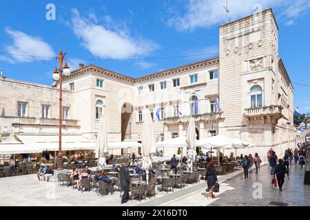 Zadar, Kroatien, 15. April 2019: Touristen sitzen auf der Terrasse eines Cafés auf dem Platz des Volkes vor dem Rathaus. Stockfoto