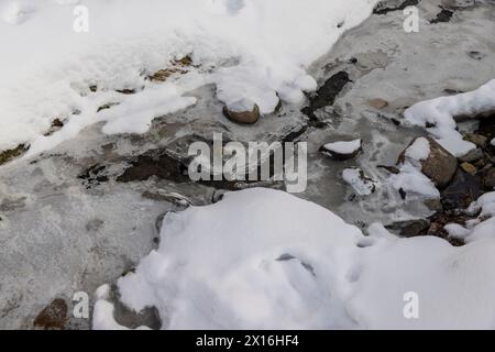 Ein schmaler kleiner Fluss im Winter, bedeckt mit Schnee und Eis, das Eis auf dem Fluss ist mit einem Kunststoff-geogitter verstärkt Stockfoto