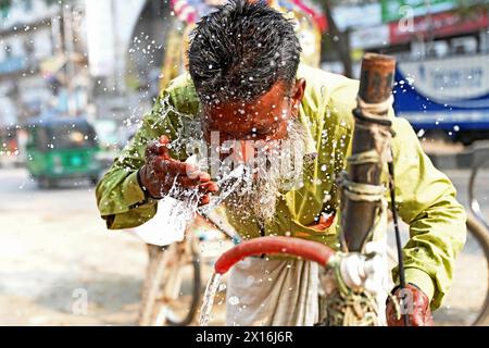 Dhaka, Bangladesch. April 2024. Ein Rikscha-Fahrer wäscht sich am 15. April 2024 an einer Wasserleitung am Straßenrand während des Hochtemperaturwetters in Dhaka, Bangladesch, das Gesicht mit Wasser Stockfoto
