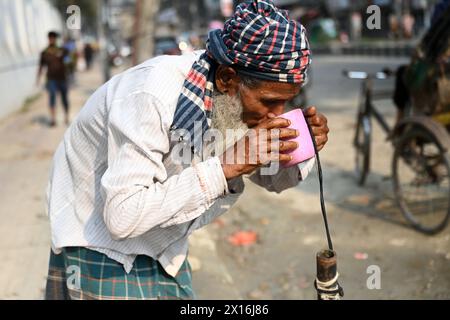 Dhaka, Bangladesch. April 2024. Ein Rikscha-Fahrer trinkt am 15. April 2024 Wasser aus einer Wasserleitung am Straßenrand während des Hochtemperaturwetters in Dhaka, Bangladesch Stockfoto