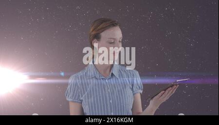 Bild einer glücklichen kaukasischen Geschäftsfrau, die ein Tablet über dem Nachthimmel mit Sternen und Licht benutzt Stockfoto Bild einer glücklichen kaukasischen Geschäftsfrau, die ein Tablet über dem Nachthimmel mit Sternen und Licht benutzt Stockfoto