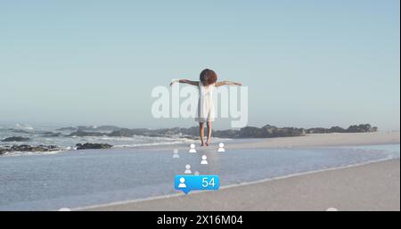 Bild von Sternen über afroamerikanerin, die am Strand die Hände erhebt Stockfoto