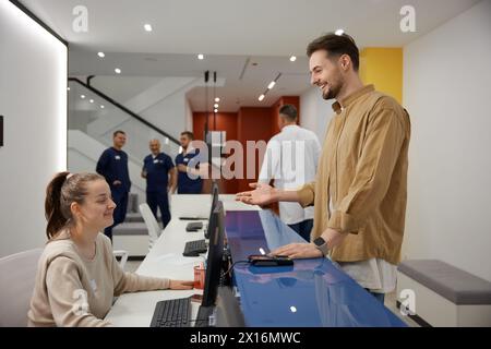 Ein Besucher spricht und lächelt mit der Krankenschwester an der Rezeption im Wartezimmer der Klinik Stockfoto