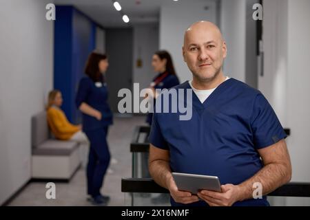 Reifer erwachsener Männerarzt in Uniform mit digitaler Tablette im Klinikkorridor Stockfoto