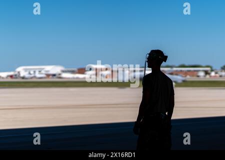 Ein Mann mit einem Headset steht auf der Landebahn und blickt über den Asphalt. Der Himmel ist klar und die Sonne scheint hell. Der Mann wartet darauf Stockfoto