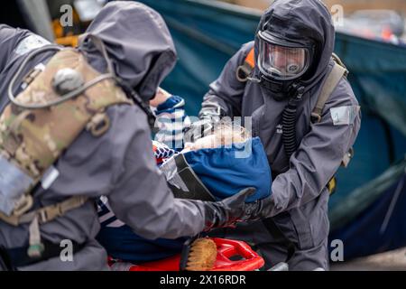 Ein Mann in einem Gefahrenanzug hilft einem Kind. Die Szene ist angespannt und ernst, da der Mann eine Gasmaske trägt und das Kind festgehalten wird Stockfoto