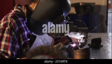 Eine Mechanikerin schweißt, während sie an einer Autowerkstatt sitzt Stockfoto