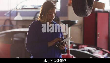 Bild von leuchtendem Licht über birassische Frau, die in der Autowerkstatt arbeitet Stockfoto