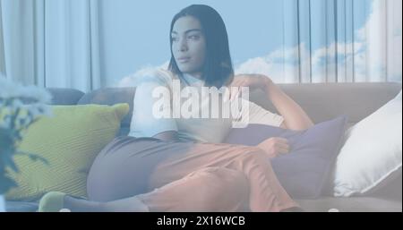 Bild des Himmels mit Wolken über einer Frau, die auf Sofa sitzt Stockfoto