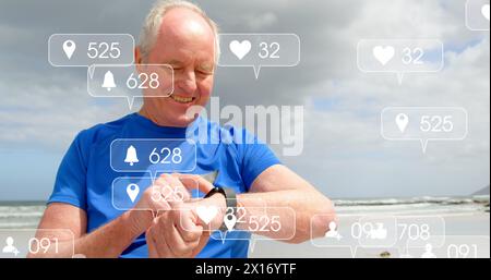 Bild von Benachrichtigungsbalken über einem älteren kaukasischen Mann, der Smartwatch am Strand benutzt Stockfoto