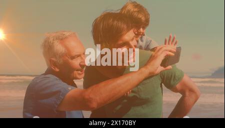 Bild von Bokeh über glücklichen Großvater, Vater und Sohn, die Selfie am Strand machen Stockfoto