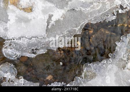 Ein schmaler kleiner Fluss im Winter, bedeckt mit Schnee und Eis, das Eis auf dem Fluss ist mit einem Kunststoff-geogitter verstärkt Stockfoto