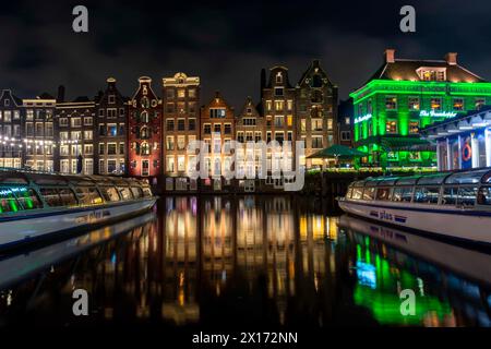 Tanzhäuser am Amsterdamer Damrak-Kanal bei Nacht. Stockfoto