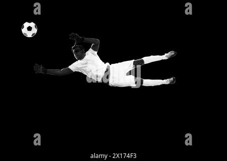 Entschlossener Sportler, Fußballspieler in Bewegung mit Ball, Training isoliert auf schwarzem Hintergrund. Schwarzweiß Stockfoto