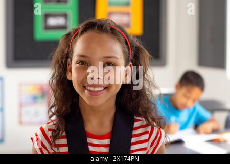 In der Schule lächelte eine junge, birassische Schülerin, die im Klassenzimmer ein gestreiftes Hemd trug Stockfoto