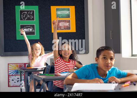 In der Schule heben verschiedene junge Schüler im Klassenzimmer die Hände, die darauf begierig sind, zu antworten Stockfoto