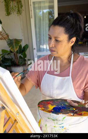 Reife, birassische Frau, die zu Hause auf Leinwand malt, fokussiert Stockfoto