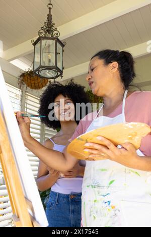 Birassische Mutter und erwachsene Tochter malen zusammen zu Hause, Mutter hält Palette Stockfoto