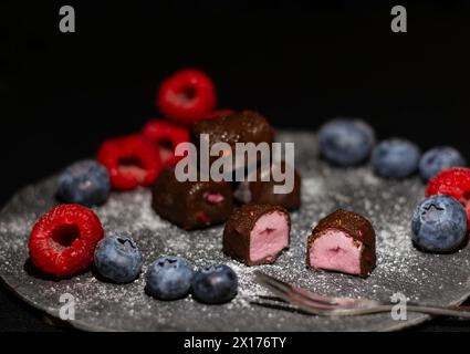 Eis mit gemischten Beeren in Schokolade mit Himbeeren und Heidelbeeren auf einer Schieferplatte Stockfoto