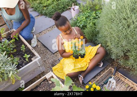 Afroamerikanerin in gelbem Kleid mit Blumen sitzt in einem Garten Stockfoto