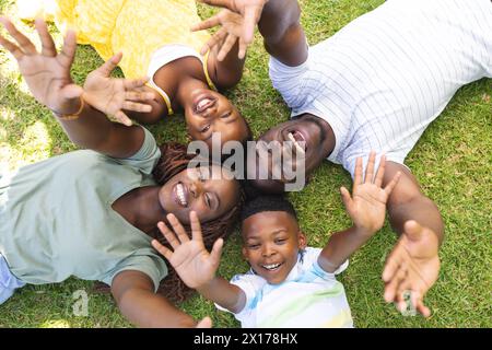 Afroamerikanische Familie liegt auf Gras, winkt vor der Kamera, genießt die gemeinsame Zeit Stockfoto