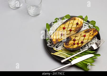 Gebackene Auberginen mit Gemüse und Reisnudeln auf schwarzer Platte. Gabel und Messer. Soße in einer Glasschale. Draufsicht Stockfoto