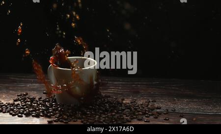 Super Zeitlupe von fallendem Eis, das in die Kaffeetasse fällt und mit schwarzem, separatem Hintergrund spritzt. Nahaufnahme des Zuckertropfens im Espresso Stockfoto