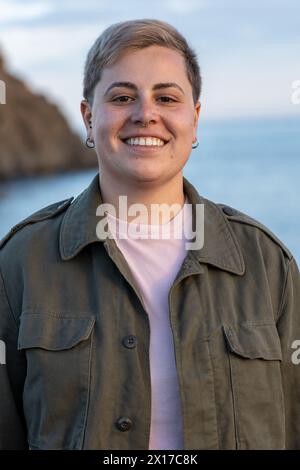 Ein strahlendes, nicht-binäres Individuum, das ein fröhliches Lächeln zeigt. Ihr kurzgefärbtes Haar unterstreicht in diesem Porträt noch mehr ihre lebendige Persönlichkeit Stockfoto