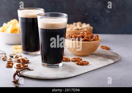 Dunkles, kräftiges Bier in hohen Gläsern mit Nüssen, Brezeln und Chips Stockfoto