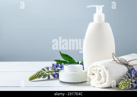 Kosmetikflasche mit Lotion und Lupinenblüten auf grauem Hintergrund. Naturkosmetik für Körper- und Gesichtspflege. Konzept der Bio-Spa-Produkte, relaxati Stockfoto