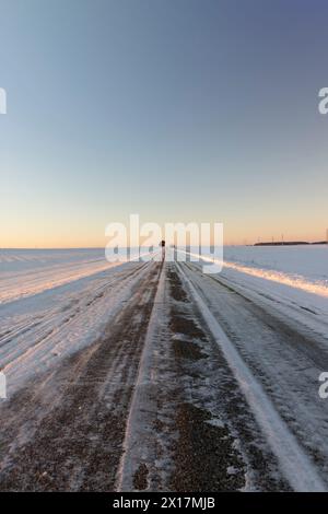 Eine schneebedeckte Straße im Winter, eine rutschige und gefährliche Straße, die bei Sonnenuntergang mit Schnee und Eis bedeckt ist Stockfoto