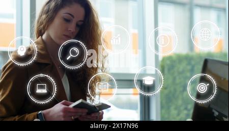 Bild mehrerer Ikonen in Kreisen über kaukasierin mit Laptop beim Lesen von Büchern Stockfoto