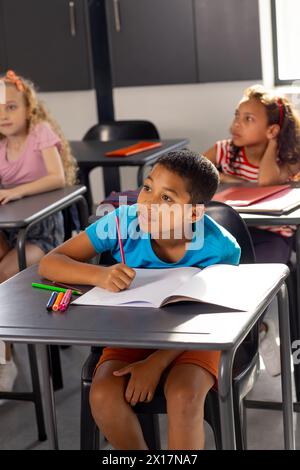 In der Schule saß ein junger männlicher Schüler an einem Schreibtisch in einem Klassenzimmer und schrieb Stockfoto