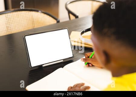 Ein afroamerikanischer Junge mit gelbem Hemd zeichnet zu Hause neben einem Tablet mit Kopierraum Stockfoto