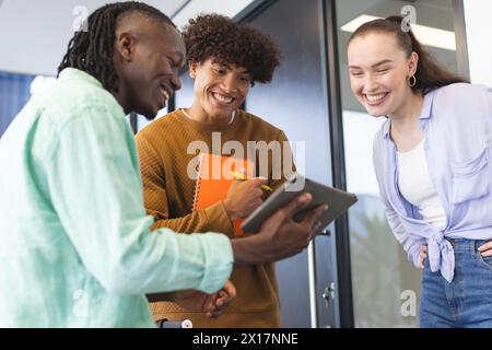 Drei junge Kollegen lachen und schauen sich ein Tablet in einem modernen Geschäftsbüro an Stockfoto
