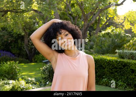 Junge Frau, die im sonnigen Garten zu Hause steht, den Hals ausdehnt, lächelt Stockfoto