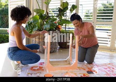 Birassische Mutter und erwachsene Tochter malen Möbel zusammen zu Hause in einem Upcycling-Projekt Stockfoto