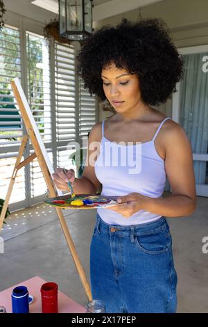 Birassische junge Frau, die zu Hause auf Leinwand malt und Farben auf Palette mischt Stockfoto