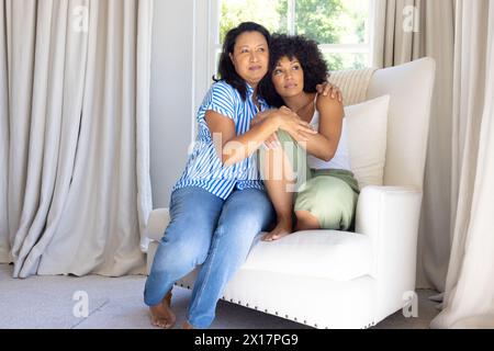 Reife Frau, die eine junge Erwachsene Tochter umarmt und beide zu Hause sitzt Stockfoto