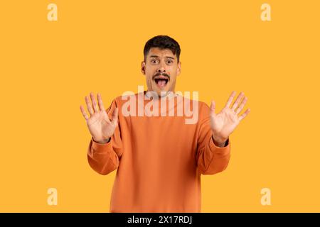 Überraschter Mann mit erhobenen Händen auf Orange Stockfoto